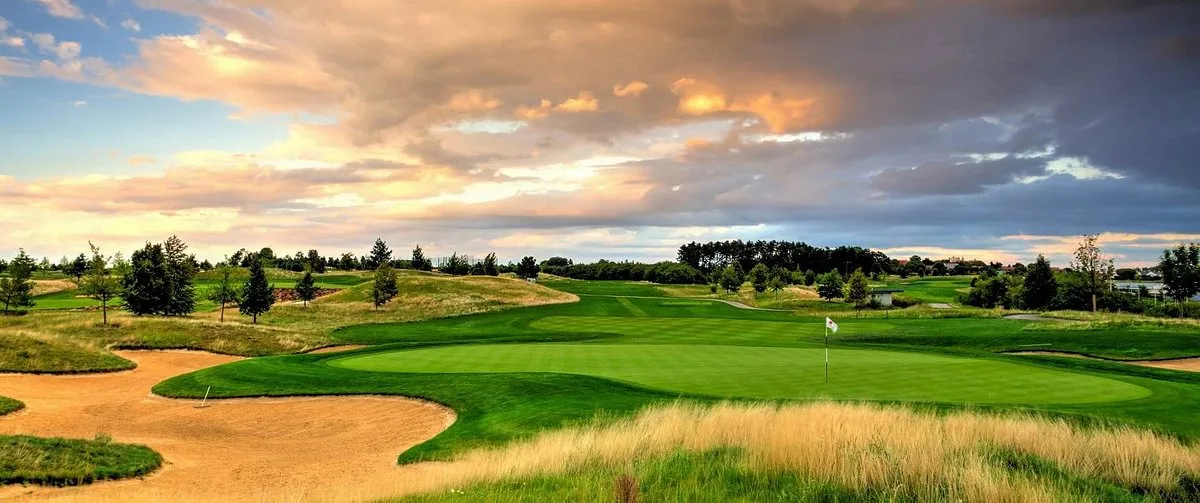 A green ringed by sandy waste bunkers and fescue at Albatross Golf Resort under a breaking sky