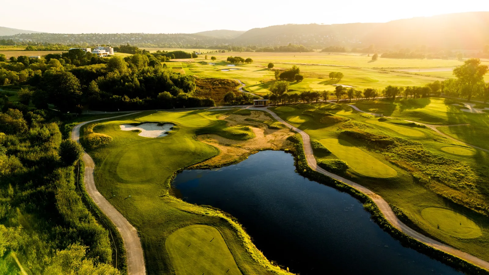 Golden-hour aerial of Prague City Golf Zbraslav, its sandy waste areas and water set in the Vltava valley