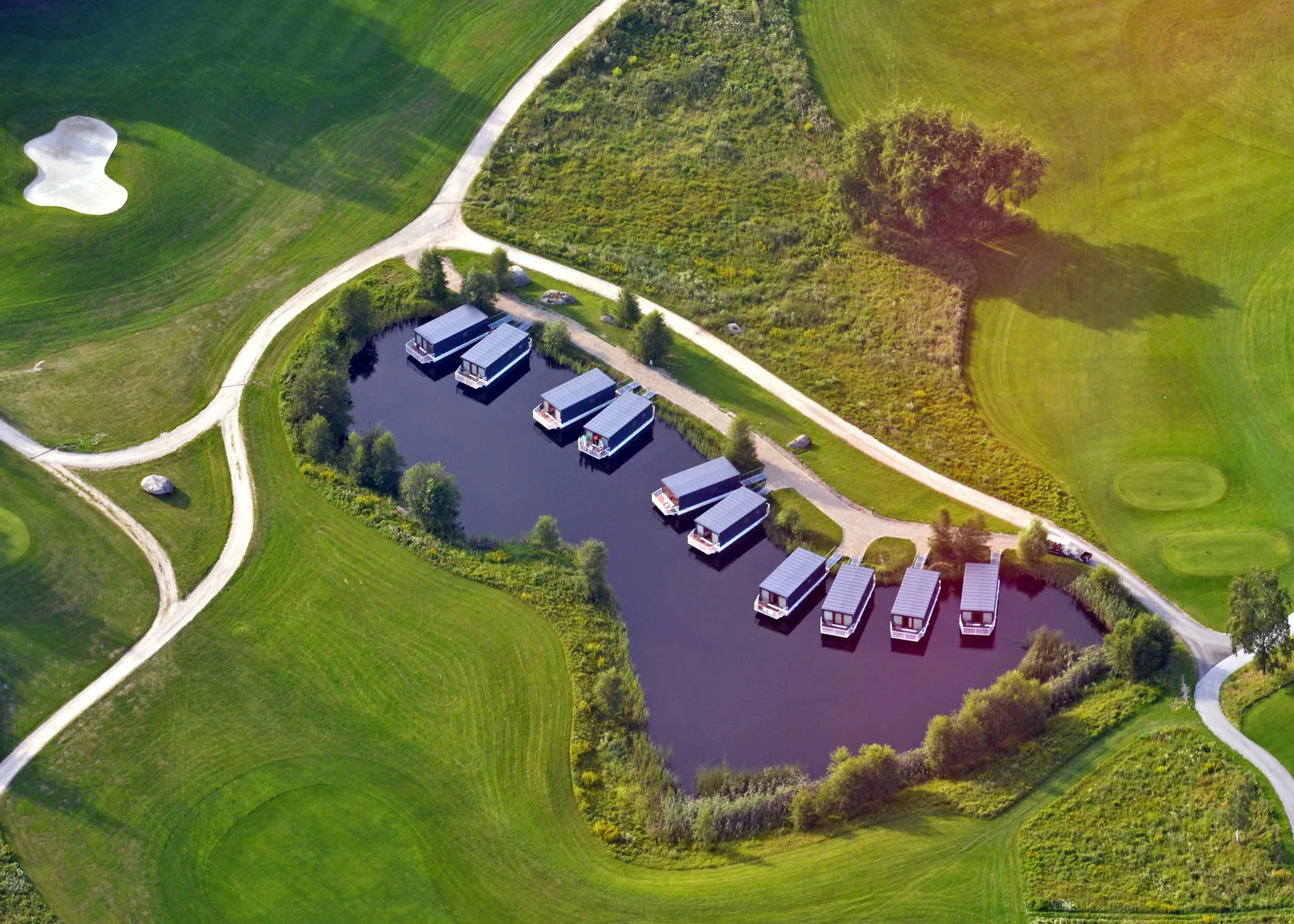 Aerial view of the houseboats moored on the lake at Ypsilon Golf Resort Liberec, ringed by the golf course